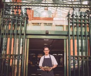 Chef standing at a restaurant entrance holding a tray of food.